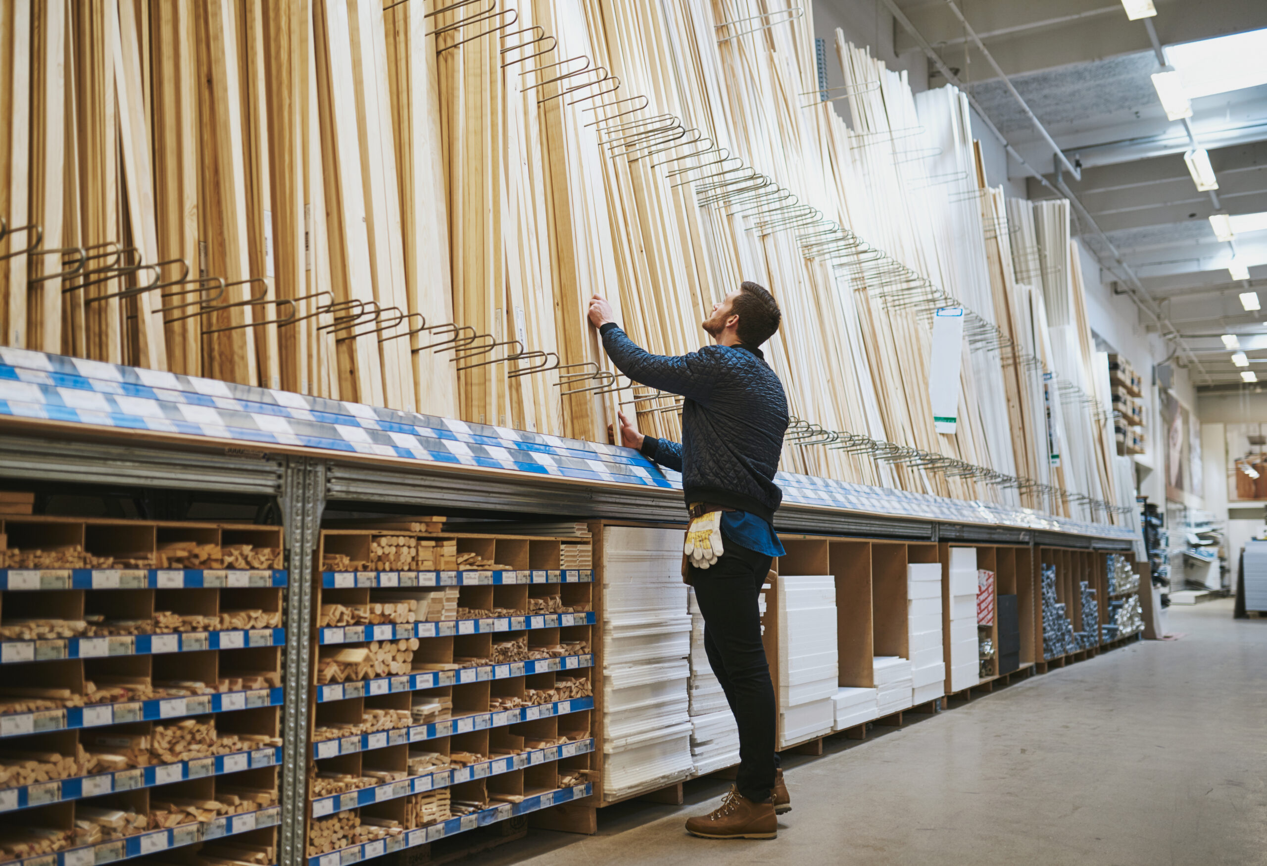 Young handyman selecting a length of cut timber from a rack in a hardware supply warehouse standing reaching up for his selection