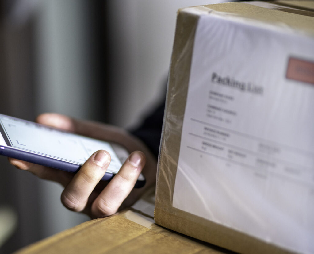Close up of a courier's hand holding smartphone for signature and cardboard boxes, copy space.